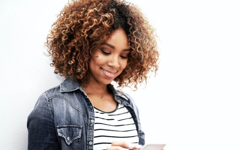 A picture of a woman smiling down at her cell phone that is in her hands.